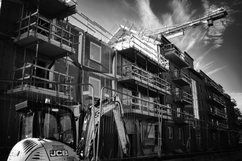 Monochrome image of a building under construction with a crane and scaffolding.